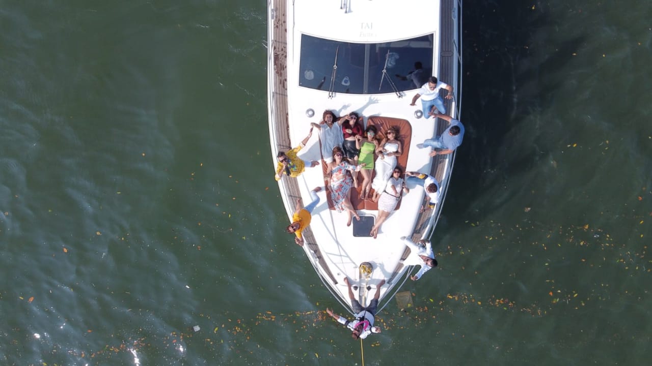 Straight-down drone view of a family lying on the bow of the Ambassador yacht with petals on the water, Goa