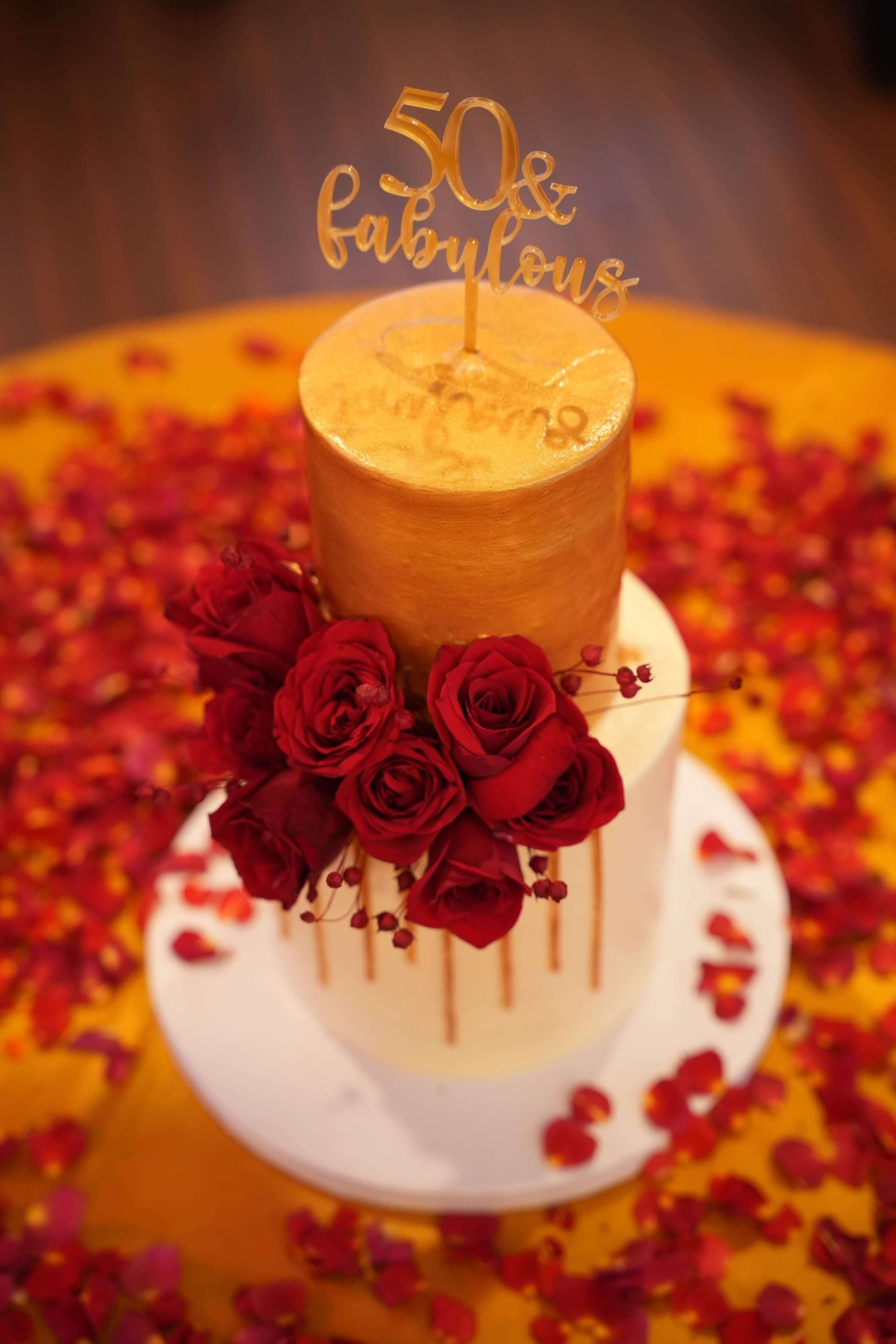 A gold milestone cake with red roses on a petal-strewn table aboard Leo Mar
