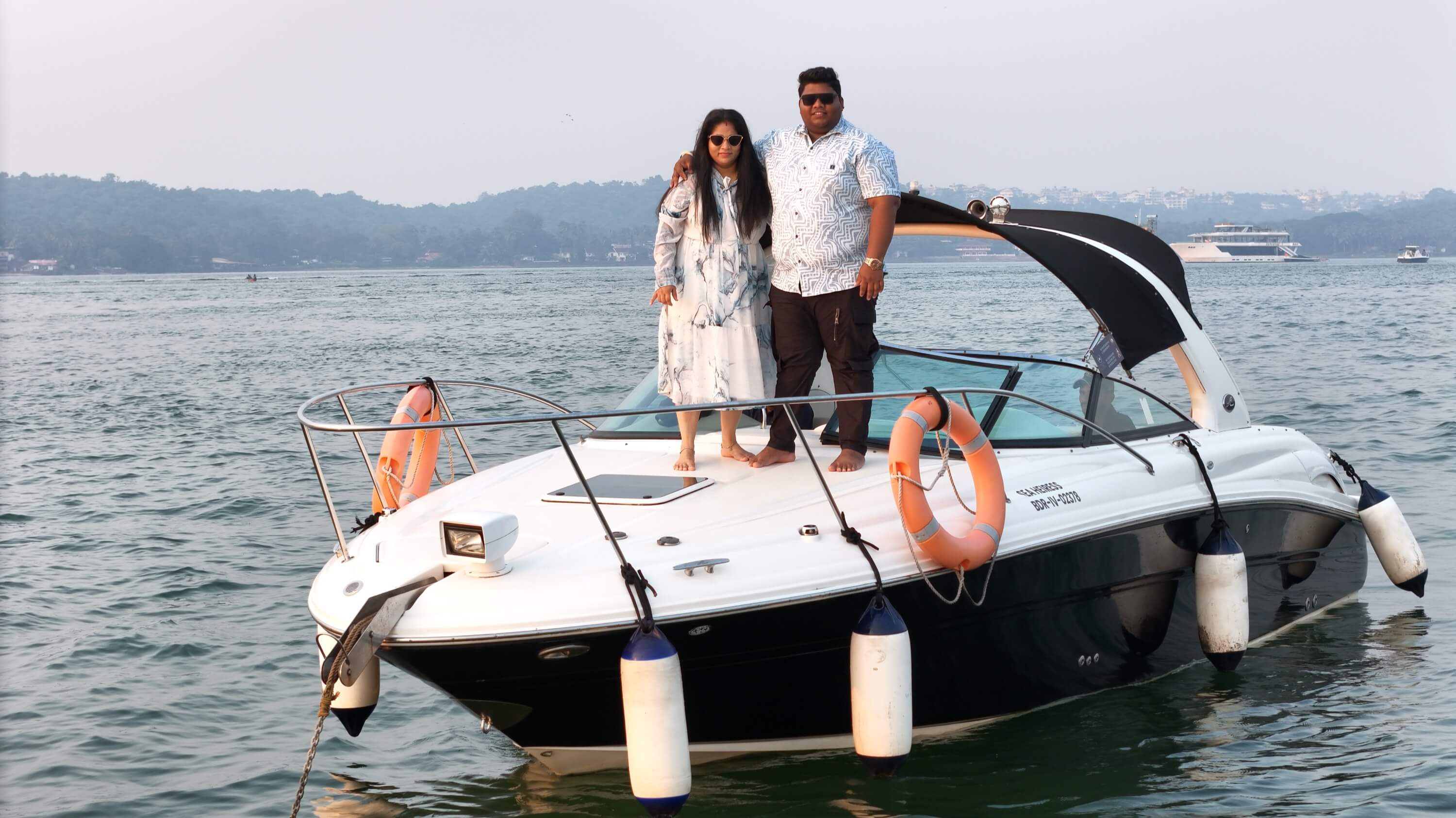 A couple standing on the open foredeck of Solstice at golden hour on the Mandovi River, Goa
